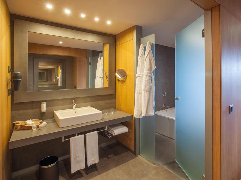 Bagno moderno con lavabo, specchio, accappatoi e vasca da bagno parzialmente nascosta.