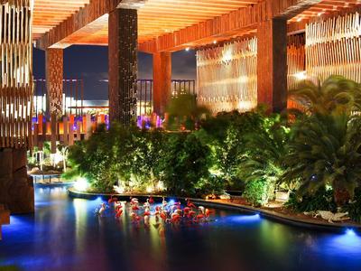 Night view of a luxurious outdoor pool area with lush greenery and vibrant city lights in the background.