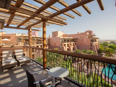 Balcony with chairs and table overlooking a resort with pool and desert-like buildings.