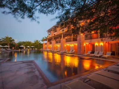 Evening view of a lit hotel pool area with lounge chairs and palm trees.
