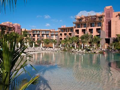 Grand complexe hôtelier avec piscine et chaises longues sous un ciel bleu et ensoleillé