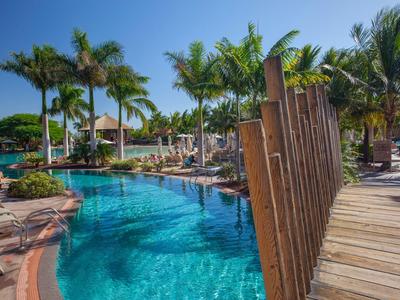 Piscine d'hôtel avec pont en bois et palmiers sous le soleil