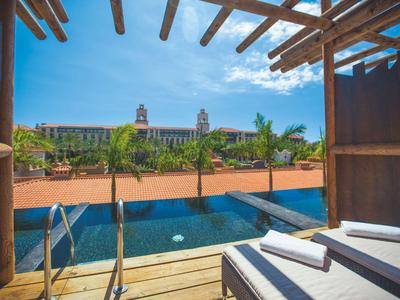 Vue depuis une terrasse avec piscine et transats sur un complexe hôtelier coloré sous un ciel bleu.