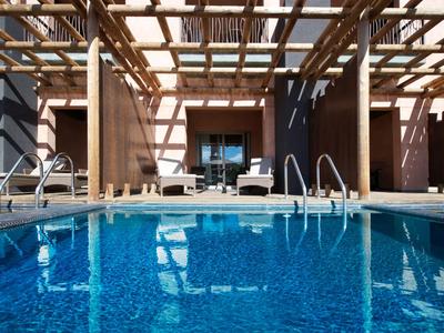 Piscine bleue claire avec pergola moderne et chaises longues dans un hôtel.