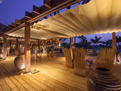 Terrazza in legno illuminata con poltrone in rattan e grandi vasi decorativi al crepuscolo.