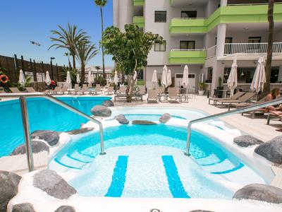 Jacuzzi z niebieskimi poduszkami obok basenu w tropikalnym kurorcie.