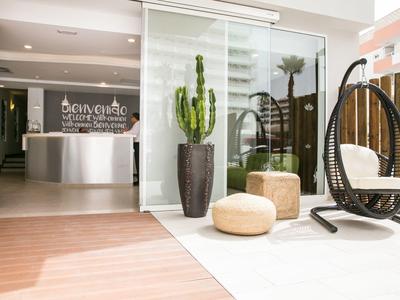 Modern hotel lobby with reception, seating area, plants, and natural light.