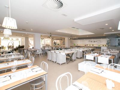 Bright, spacious hotel dining room with modern white furniture, large windows, and pendant lighting.