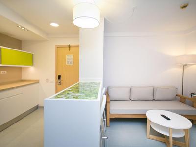 Bright hotel room with kitchenette, sofa, round table, and soft lighting.