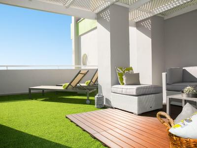Sunny hotel patio with artificial grass, loungers, and comfortable outdoor seating under shade.