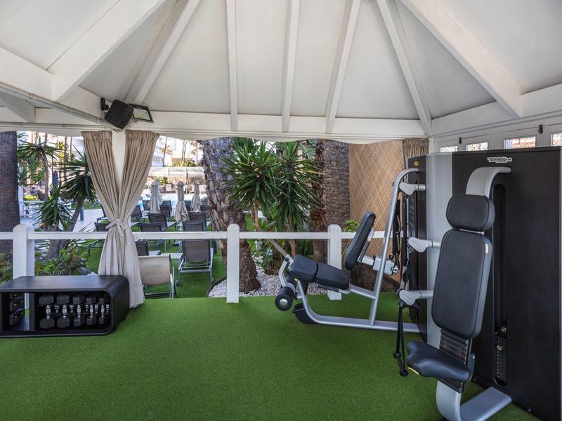 Indoor gym with green flooring, weight machine, dumbbells, and natural light from large windows.