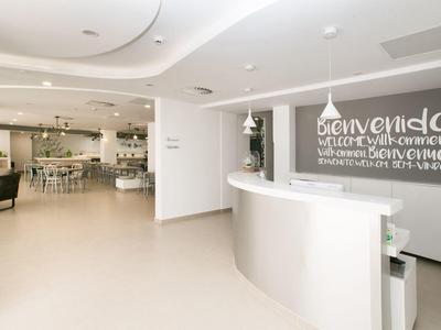 Bright hotel lobby with white curved reception desk and welcoming sign on wall.
