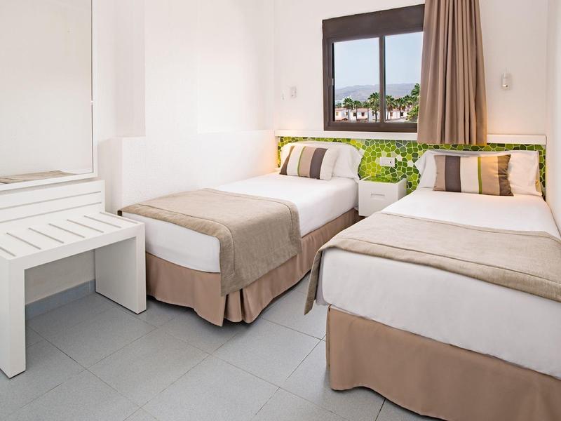 Bright hotel room with two single beds, white walls, and a window with a scenic view.