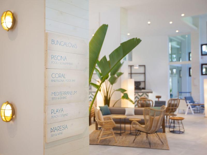 Modern hotel lobby with seating, plants, and a white board with menu items.