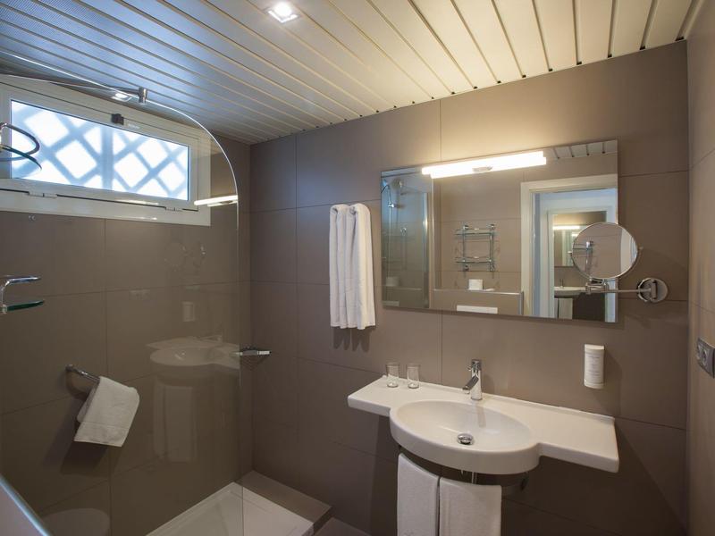 Modern hotel bathroom with brown tiles, white sink, large mirror, and towel rack.