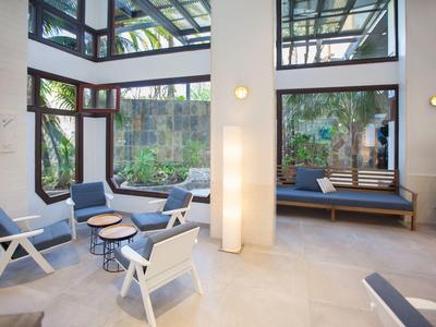 Modern lounge area with white chairs, small tables, and large windows showing greenery.
