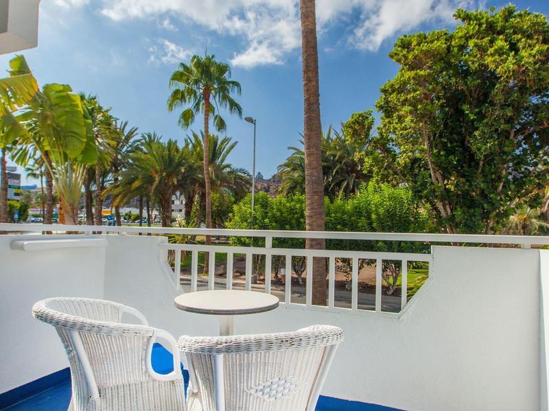 Balcony with white chairs and table overlooking palm trees under a blue sky