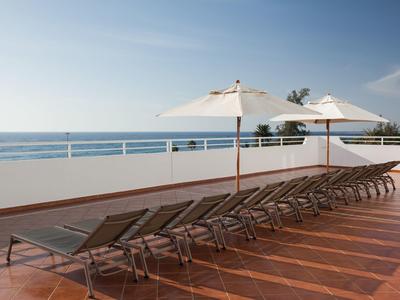 Row of lounge chairs with white umbrellas on hotel terrace overlooking the sea.