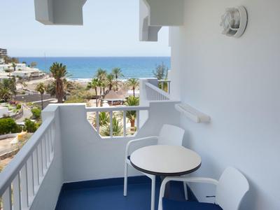 Petit balcon avec table et chaises donnant sur des palmiers et l'océan.