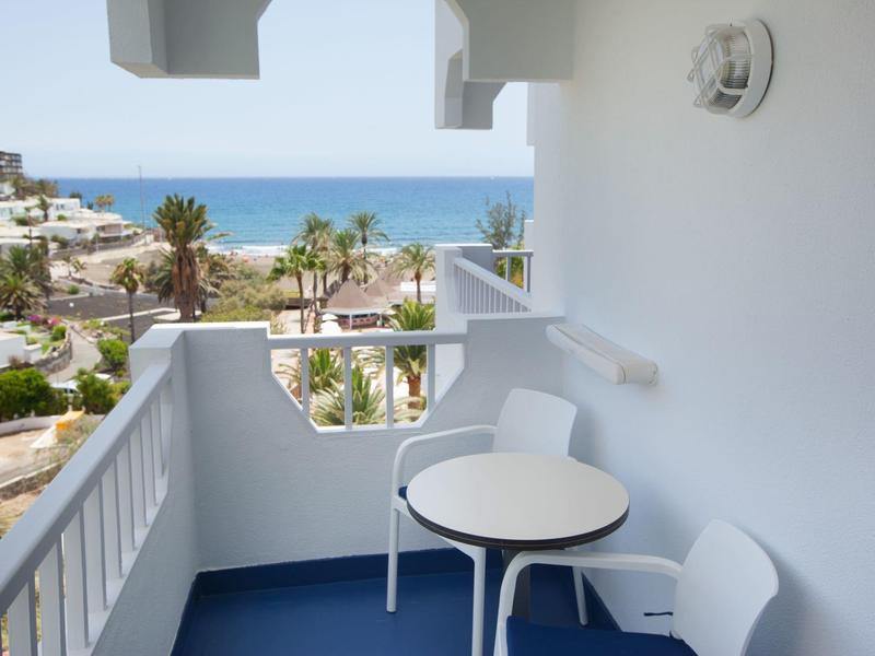 Balkon mit weißem Tisch und Stühlen, Blick auf Palmen und das blaue Meer.