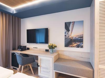 Moderner Arbeitsbereich mit Holzschreibtisch, grauem Stuhl, Fernseher und Sitzbank neben Fenster.