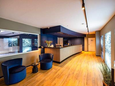 Moderner Empfangsbereich mit dunkelblauem Tresen, Holzfußboden und zwei blauen Sesseln.