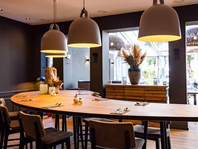 Moderner Essbereich mit langem Holztisch, schwarzen Stühlen und großen Hängeleuchten in warmem Licht.