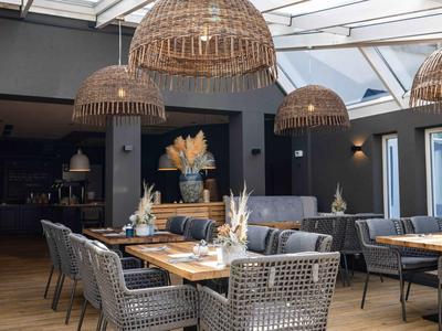 Modernes Restaurant mit runden Holztischen, grauen Stühlen und großen geflochtenen Lampenschirmen.