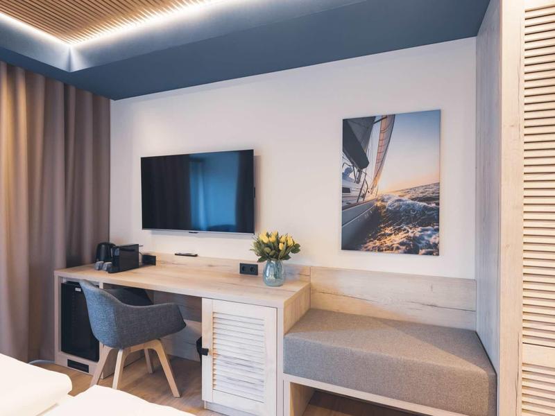 Moderner Arbeitsbereich mit Holzschreibtisch, grauem Stuhl, Fernseher und Sitzbank neben Fenster.