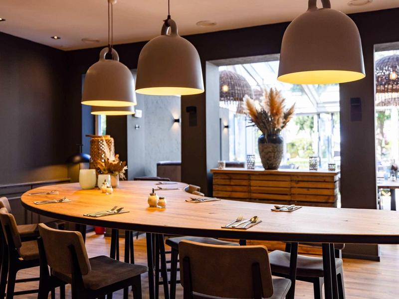 Moderner Essbereich mit langem Holztisch, schwarzen Stühlen und großen Hängeleuchten in warmem Licht.