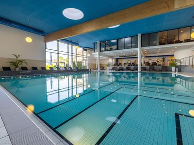 Innenbereich mit großem Schwimmbecken, modernen Holzdeckenbalken und großen Fenstern in einem Hotel.