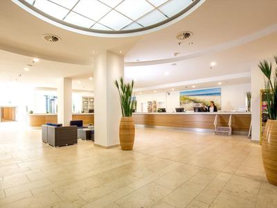 Helle, moderne Hotellobby mit Rezeption, Sitzbereichen und großen Pflanzen in Töpfen.