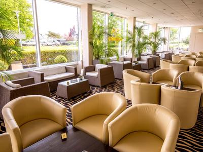 Helle Hotellounge mit bequemen beigen Sesseln und großen Fenstern mit Außenblick.