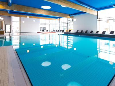 Innenhoteleigener Pool mit blauen Wänden, großen Fenstern und Liegestühlen am Beckenrand.