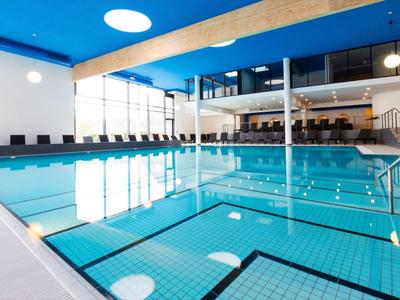 Moderner Innenpool mit großer Glasfront, blauer Decke und Holzakzenten in einem Hotel.