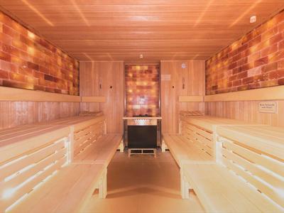 Innere Holzsauna mit zwei Holzliegen und einem Herd in der Mitte.