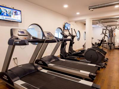 Moderner Fitnessraum mit Laufbändern, Crosstrainern und Kraftgeräten auf Holzboden.