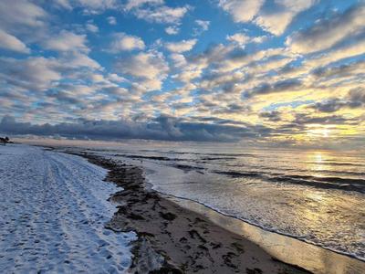 Strand mit Schnee und bewölktem Himmel während des Sonnenaufgangs.