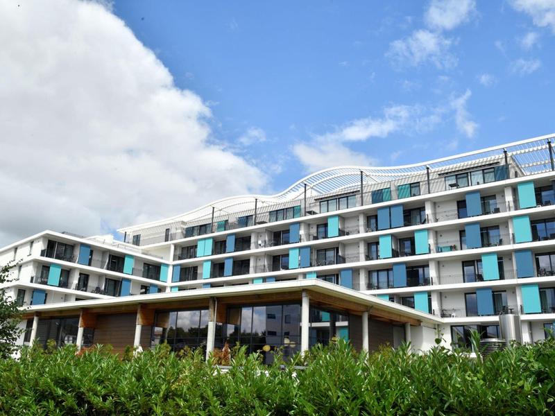 Modernes mehrstöckiges Hotel mit Glasfassade und großer Terrasse unter blauem Himmel.