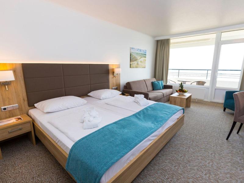 Modernes Hotelzimmer mit zwei Betten, Sitzbereich und großem Fenster mit Meerblick.