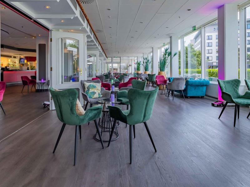 Moderner Hotel-Loungebereich mit bunten Sesseln und großen Fenstern mit Blick auf Stadtgebäude.