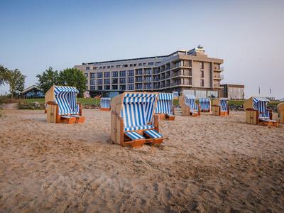 Strand mit typischen Strandkörben vor einem mehrstöckigen Hotelgebäude bei klarem Himmel.