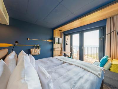 Chambre moderne avec grand lit, mur bleu et balcon avec vue sur la mer.