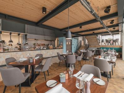 Moderně zařízená restaurace s dřevěnou podlahou a šedými židlemi pod dřevěným stropem.