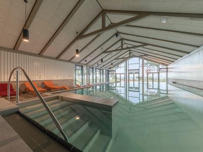 Piscine intérieure moderne avec escaliers, façade en verre et espaces détente dans un hôtel.