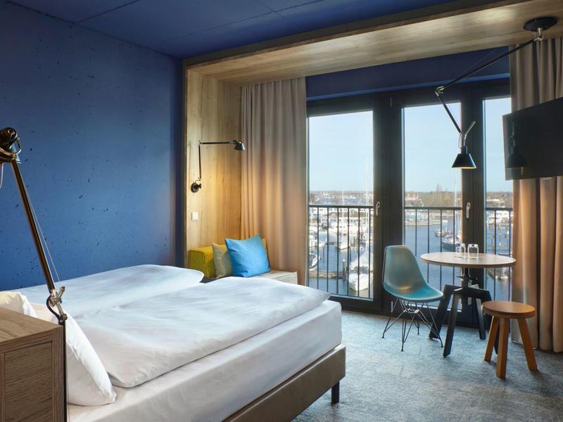 Chambre d'hôtel confortable avec grand lit, mur bleu et balcon donnant sur la ville.
