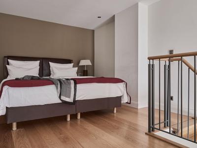 Modernes Schlafzimmer mit zwei Einzelbetten und Holzboden neben einer Treppe.