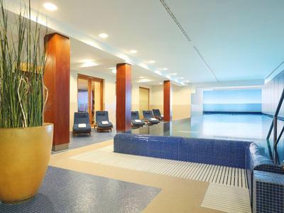 Moderner Hotelpoolbereich mit blauen Fliesen und Sitzgelegenheiten in einem hellen Raum