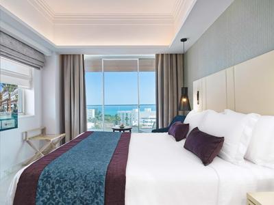 Modernes Hotelzimmer mit großem Bett, Meerblick, hellen Wänden und stilvoller Dekoration.