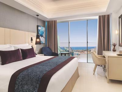 Modern hotel room with large bed, balcony, and sea view